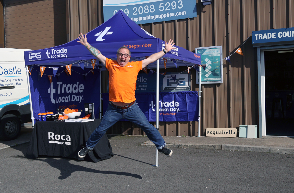 Trade Local Day brand ambassador Mark Millar jumping in the air from excitement in front of Trade Local Day merchandise stand, all on Trade Local Day the 9th of September.